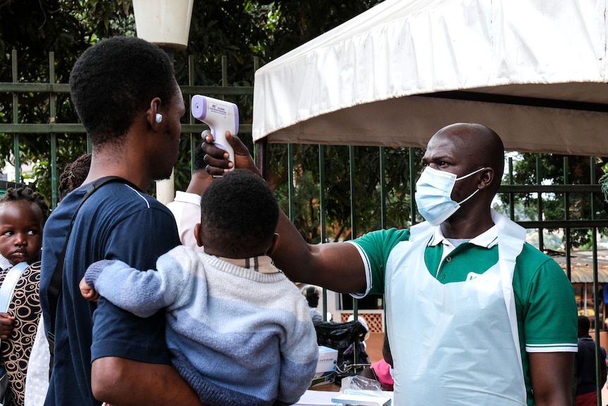 A health official uses a thermometer to screen people in front of Kibuli Muslim Hospital in Kampala, Uganda