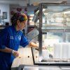 Great Valley School District culinary coordinator Jenifer Halin cleans up the salad bar in the cafeteria at Great Valley High School in Malvern, Pennsylvania. She is wearing a blue chef's coat and has a rainbow bandanna on her head.