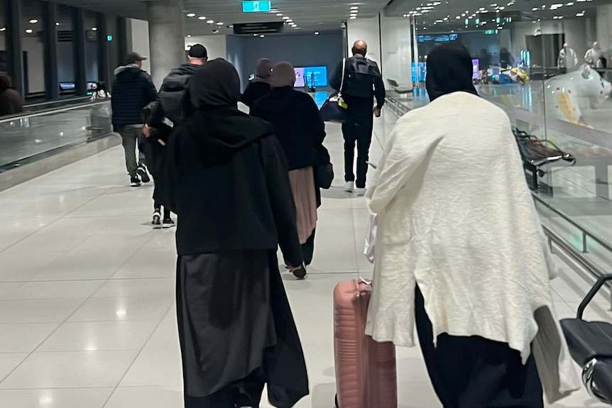 Two women wearing hijabs roll suitcases through an airport terminal