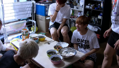 The seven members of BTS lived together in one home as trainees, sharing a single bathroom. The members prepare a meal together in a living room crowded with household items, including a drying rack. Courtesy of BigHit Music