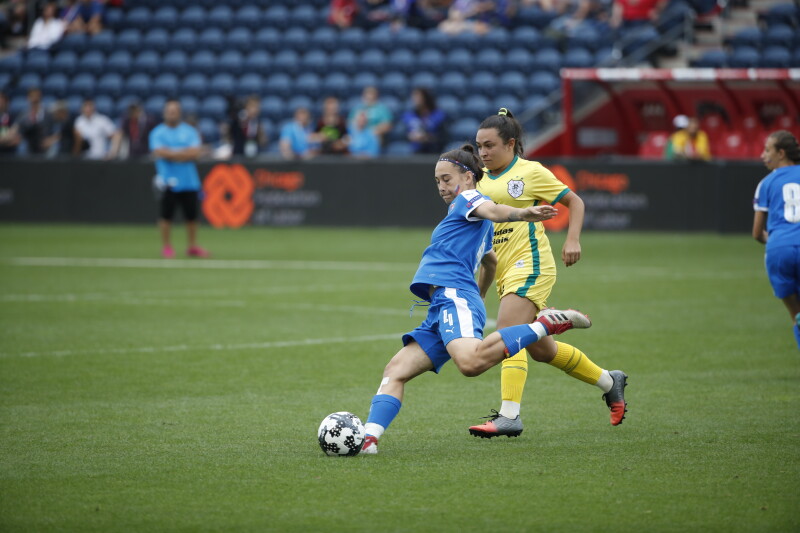 Two female players from opposing teams, one draws back her foot in preparation to kick the football.