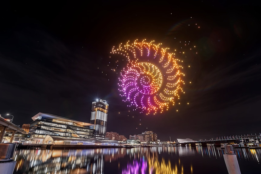 Colourful drones make a shell pattern above sydney harbour.