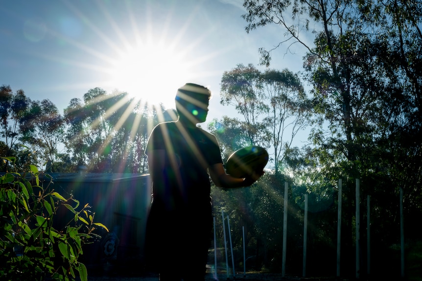 A silhouette photo of a young boy playing AFL in the backyard