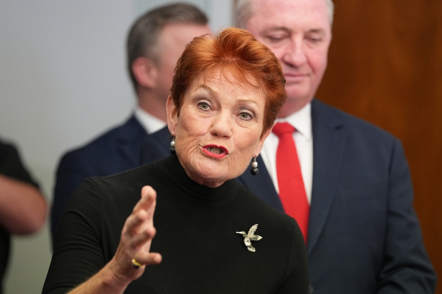 A woman with red hair speaks directly toward the camera