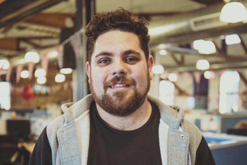A man in a dark shirt and hoodie smiling at the camera