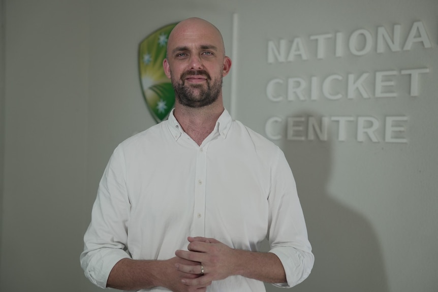 a man stands in front of the logo of the National Cricket Centre