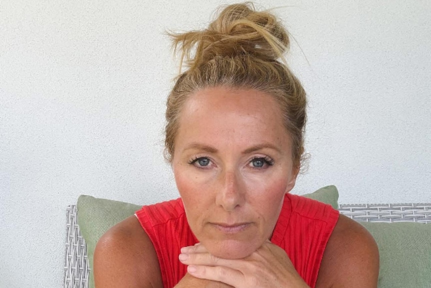 A middle aged woman looking sadly at the camera with her chin in her folded hands