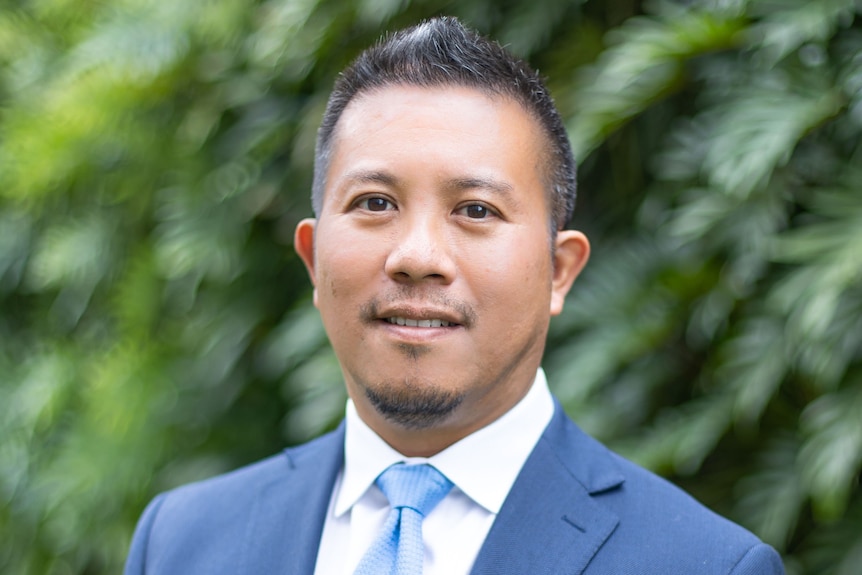 A man wearing navy suits and smiling to the camera.