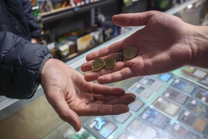 A customer gives a store owner coins as a form of payment in a trarding card shop