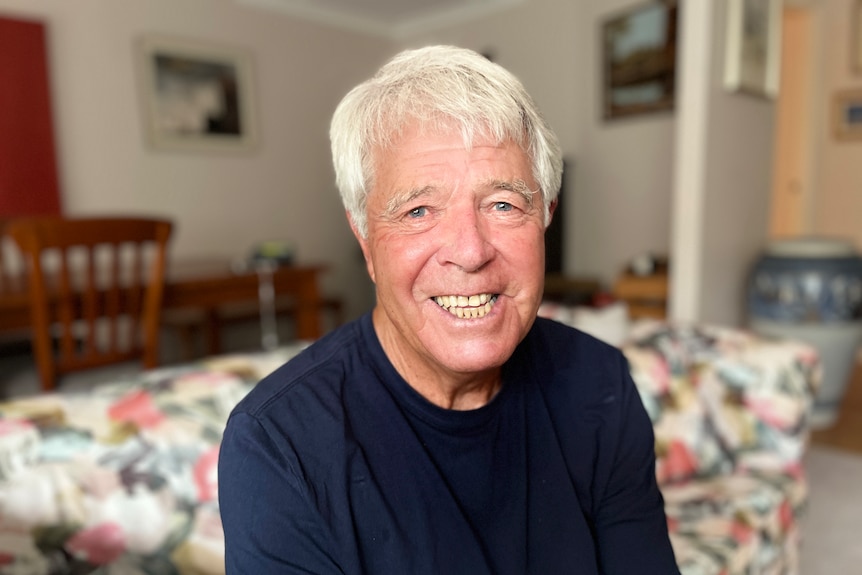 A man sits smiling on a couch