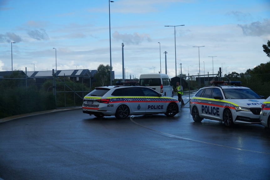 a white van enters through a wire gate as police cars standby