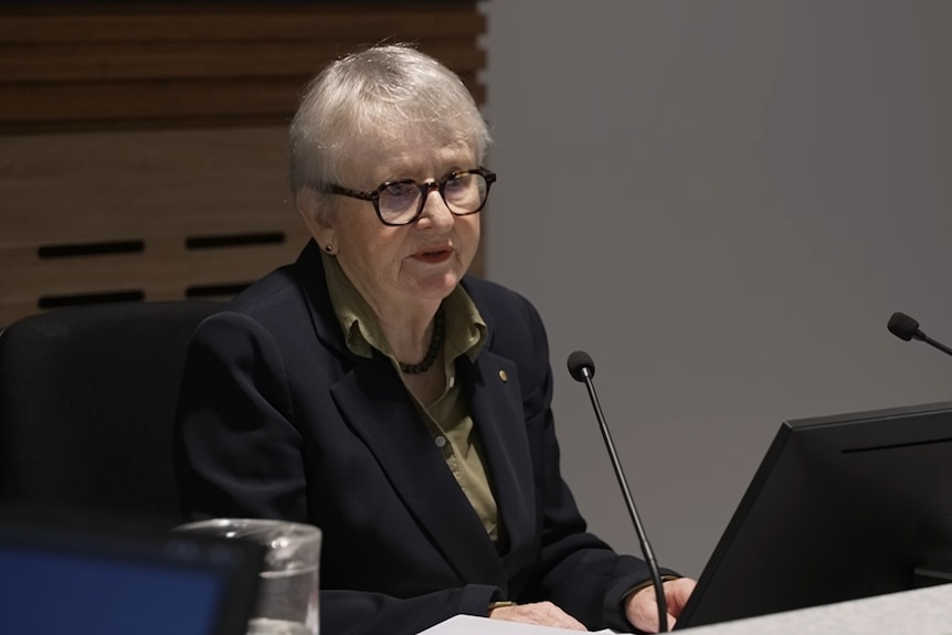 Woman sits at bench speaking into microphone