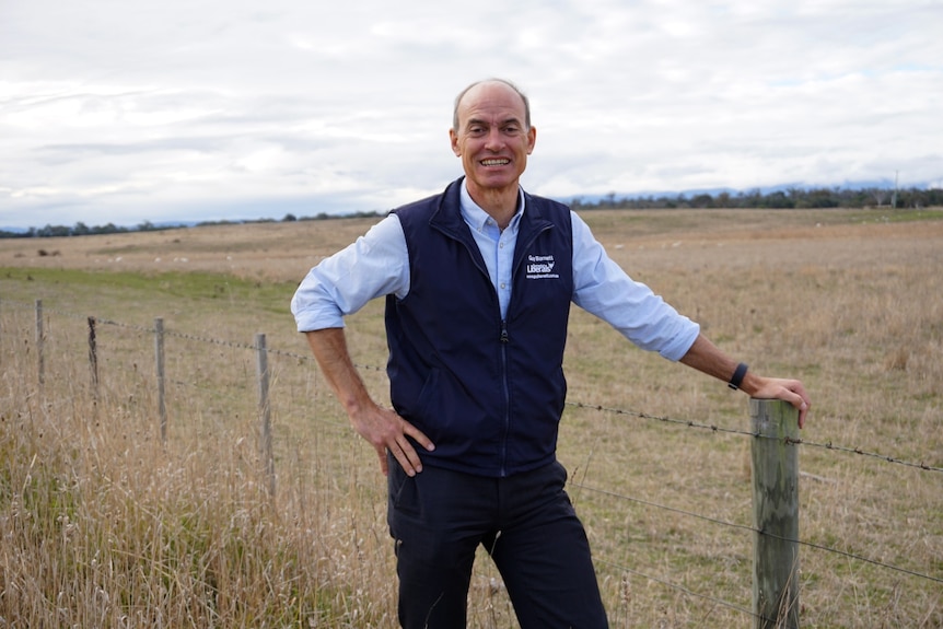 Guy Barnett standing in a paddock, leaning on a fence post.