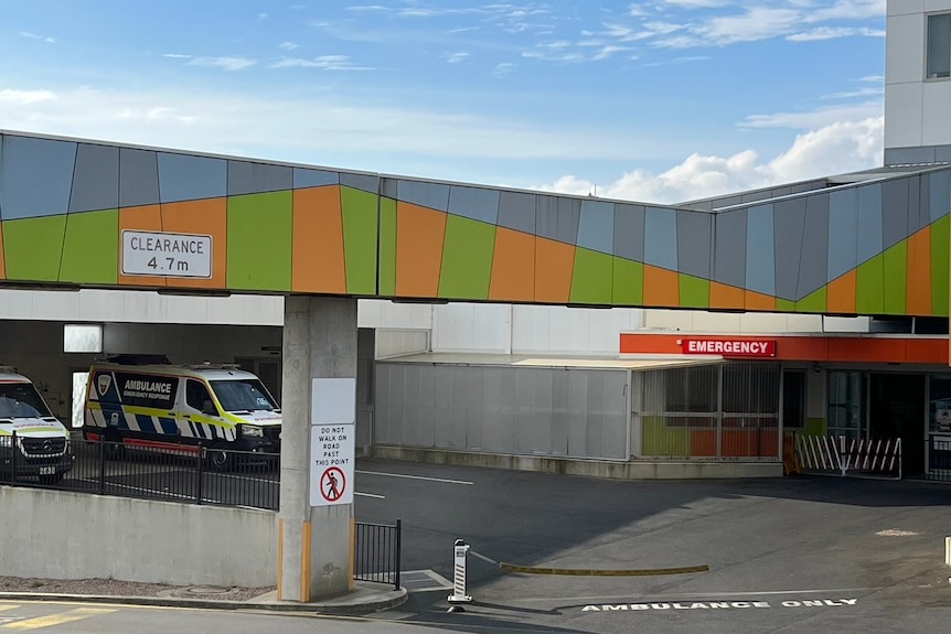 an ambulance sits in a driveway in front of an emergency sign with bright orange and green panels above
