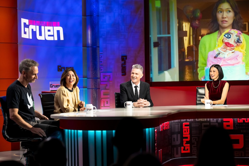 The panel sit around a desk on the set of Gruen.