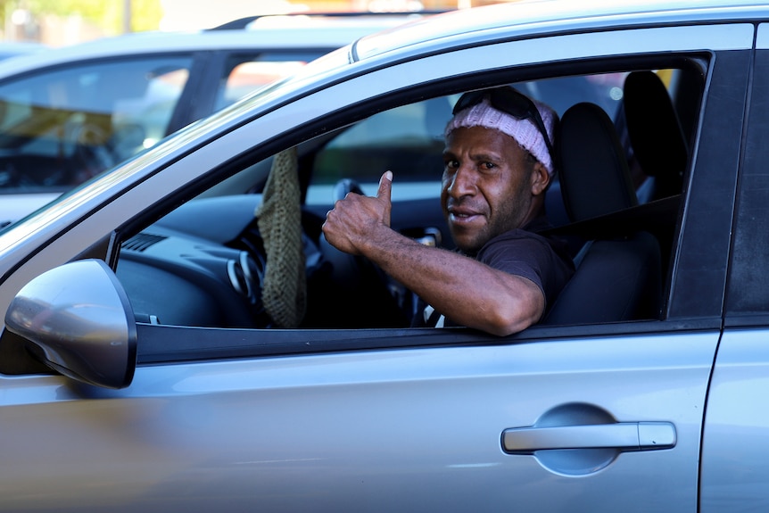 A Pacific Islander worker gives a thumbs up while sitting in a parked car 