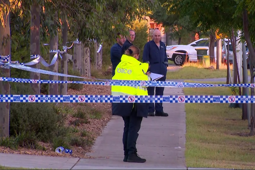 Multiple rows of blue and white police tape stretch across a residential footpath where police stand.