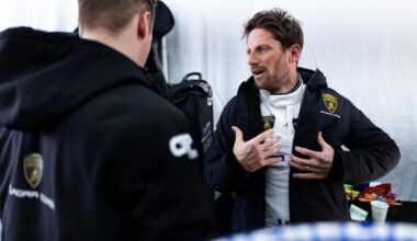 Romain Grosjean puts his jacket on in a motor garage