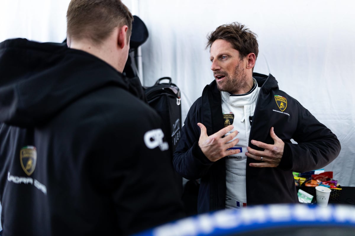Romain Grosjean puts his jacket on in a motor garage