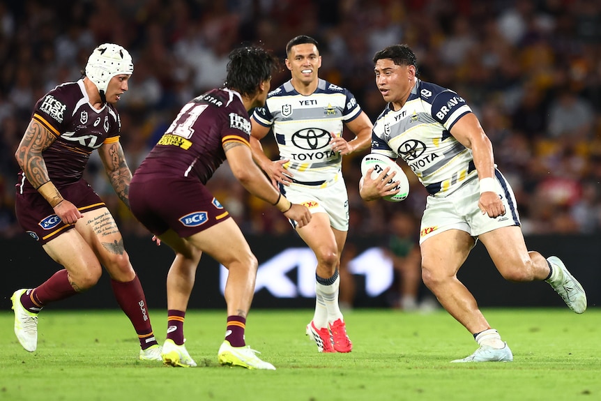 Jason runs the ball during a rugby league match, surrounded by other players.