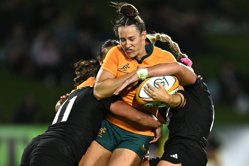 a Wallaroos player is tackled b y Black Ferns opponents.