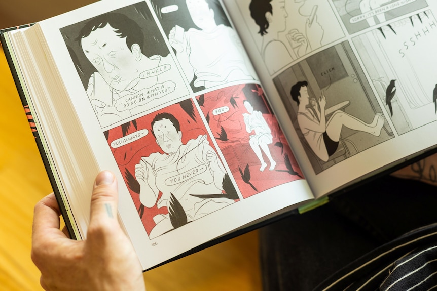 A person's hands holding open a graphic novel, displaying the illustrated panels.