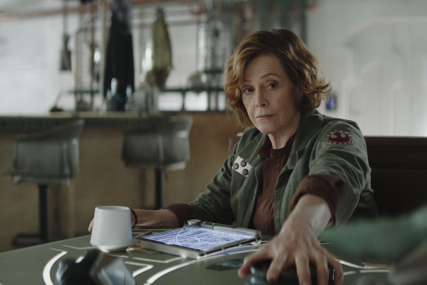 A woman sits at a table with a tablet and a coffee mug