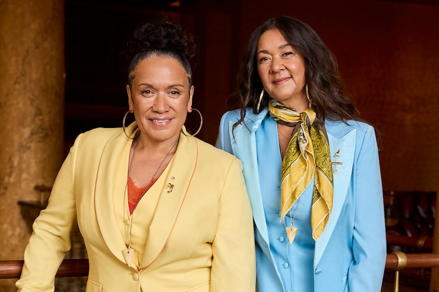 Two Tongan-Australian women pose in floral power suits, daisy yellow and powder blue respectively, on a marbled balcony