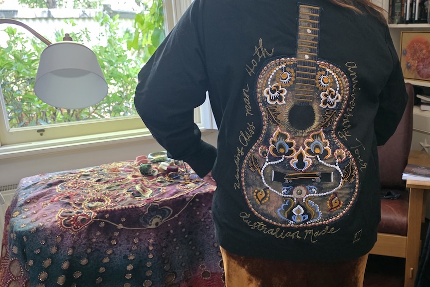 A lady wearing a jacket with guitar painted on the back.