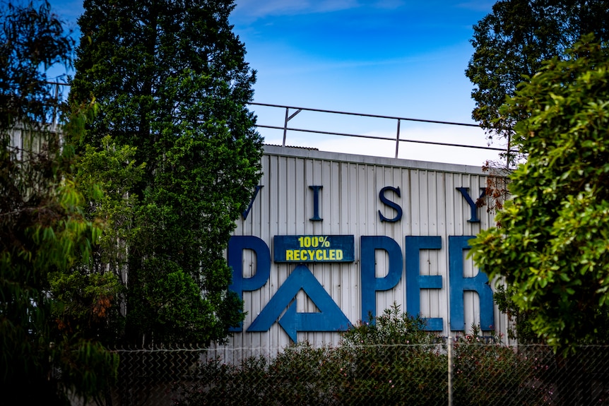 Blue letters on the side of a white corrugated iron building say "Visy Paper" and "100 per cent recycled".