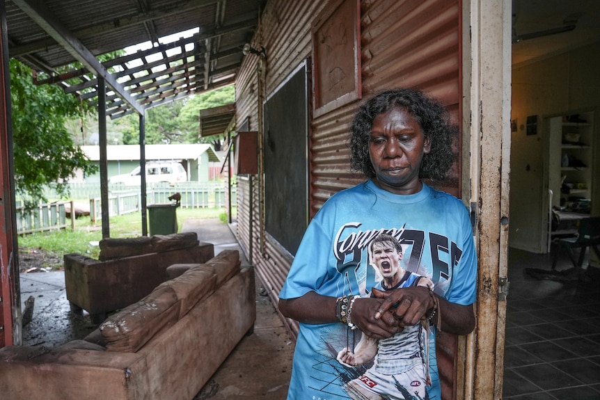 An Aboriginal woman leaning up against the outside wall of house