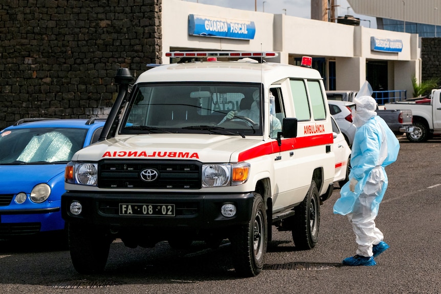 A person in protective clothing speaks to the driver of an ambulance.