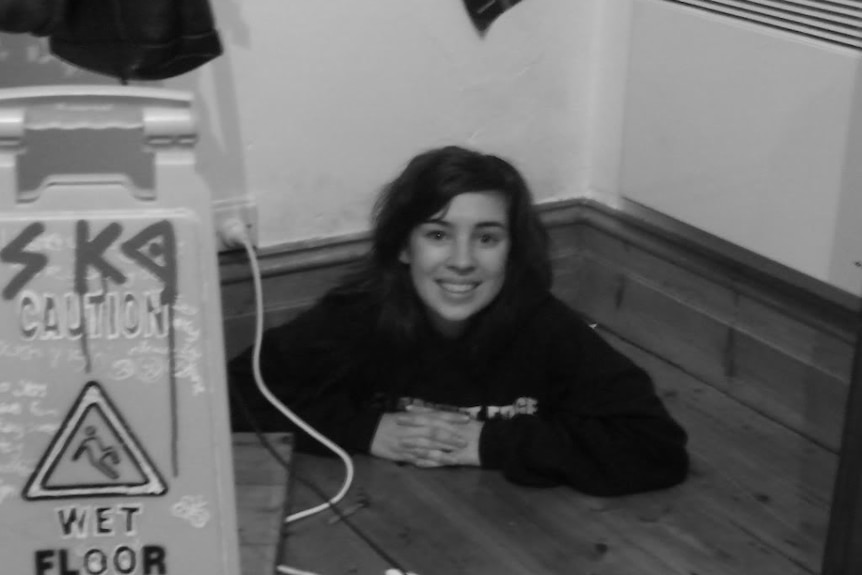 Black and white photo of a smiling woman's face coming out of the floor. Caution sign beside her