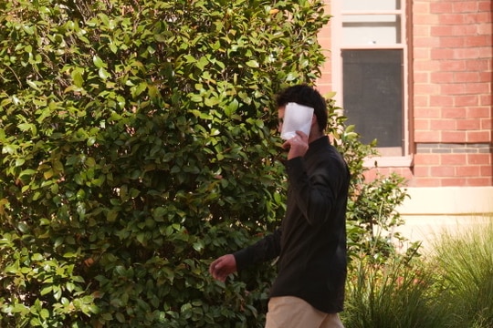 A man with dark hair holds a piece of paper against his face