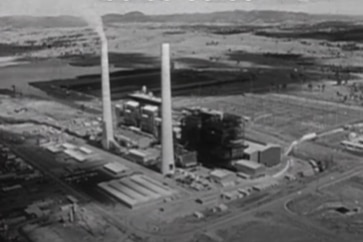 A black-and-white image of a power station with two tall chimneys.