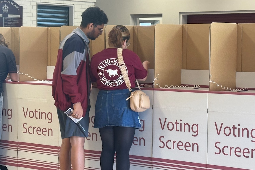 Two people in maroon tops standing at a voting booth.