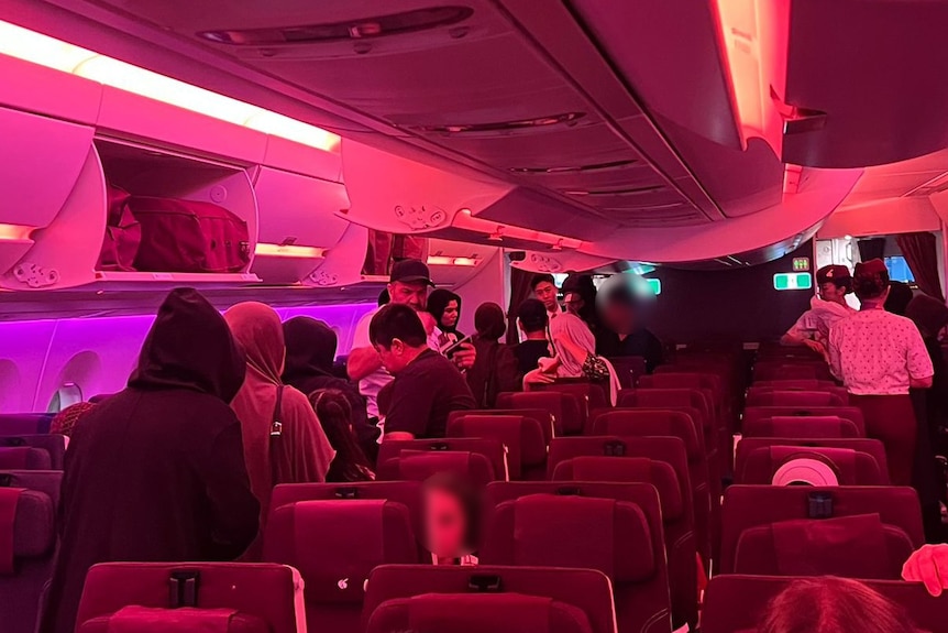 A group of women wearing hijabs stand in an aeroplane aisle