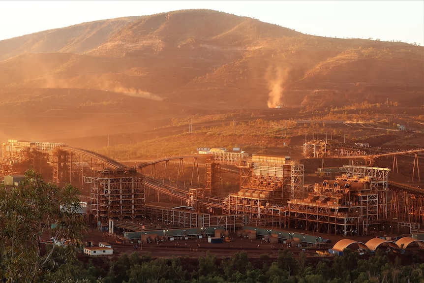 A mine with structures and red dirt in front of a a hill.
