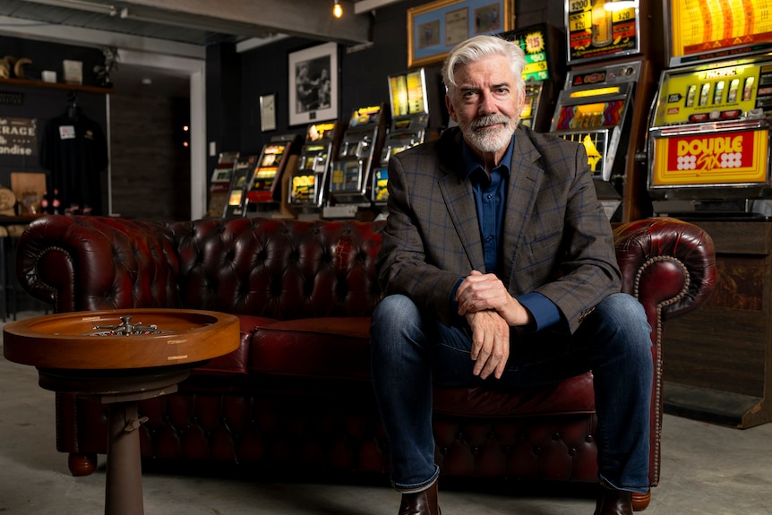 A man sits in front of a row of pokie machines