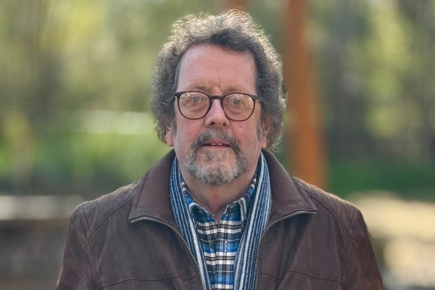Scott Goddard wears glasses, a brown jacket and a check shirt