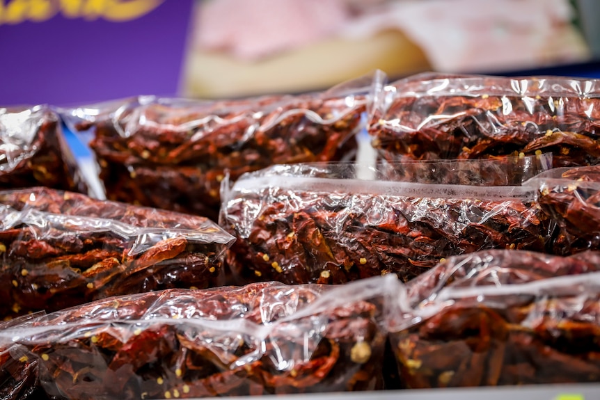 Plastic sealed bags of dried red chillies piled on a supermarket shelf 