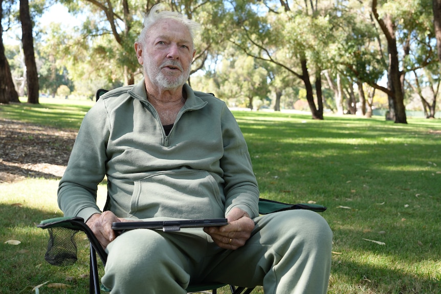 A man in a green tracksuit sits outside in a shady park
