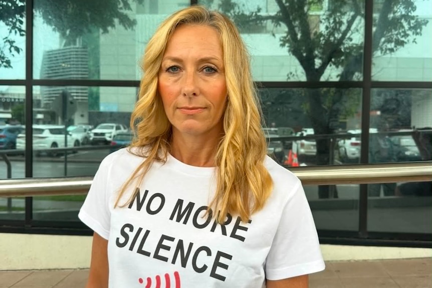 A middle aged woman outside of court wearing a shirt which reads no more silence
