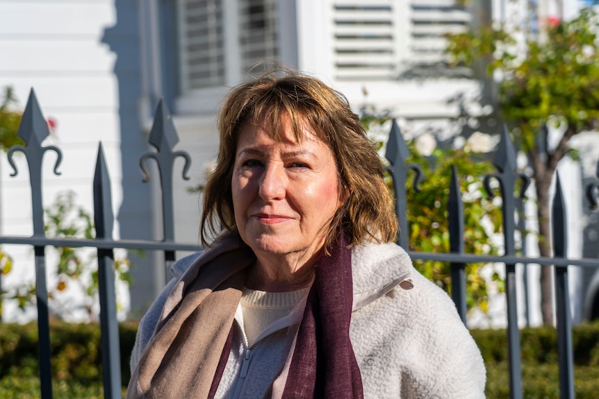 A woman with brown hair and white jumper and coloured scarf in the street
