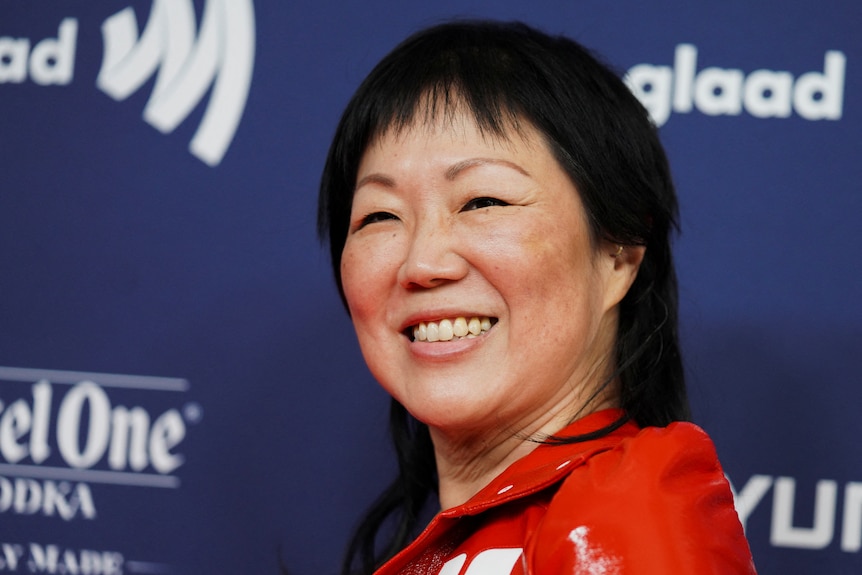 A woman in red smiles in a close up.