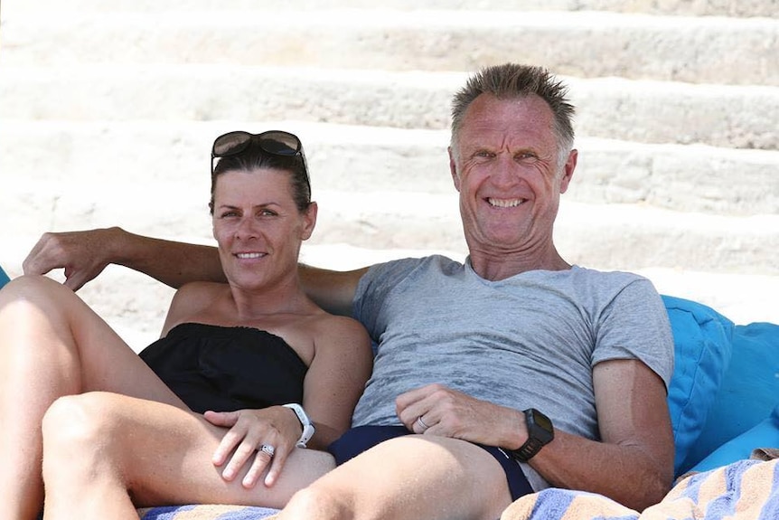 A man and woman sitting on towels at a beach.