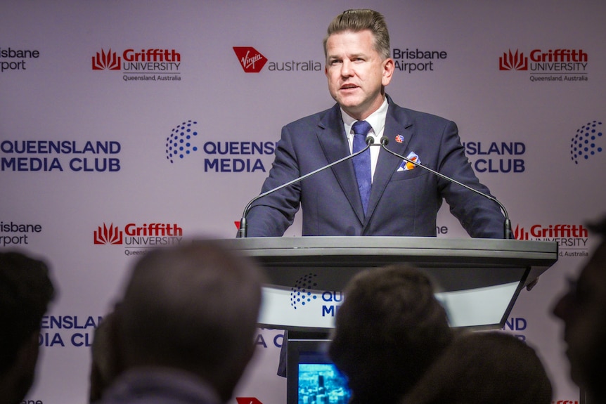 Man in a suit speaking at a lectern.