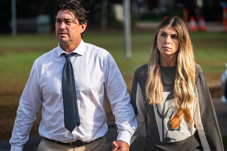 A man in a shirt and tie walking with a woman with long hair.