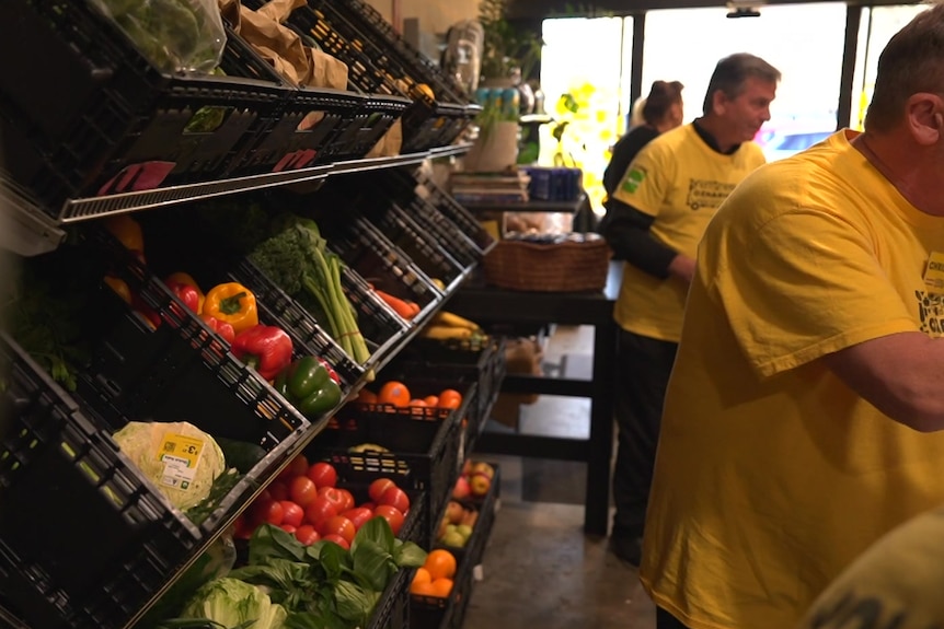 Groceries against wall of market with volunteers handing produce to customers.