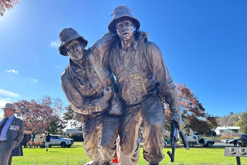 a bronze statue of two men in army uniforms, one carrying the other in a park